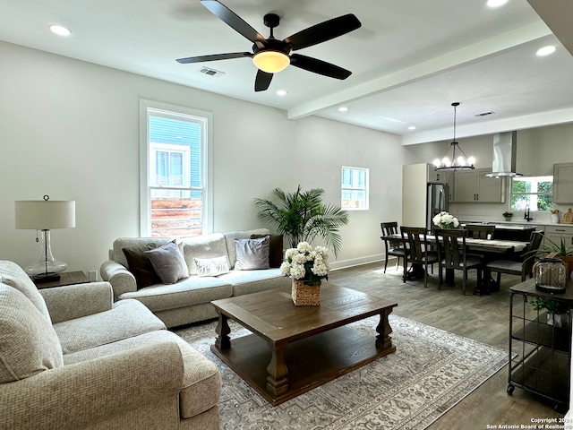 living room with light wood-type flooring, ceiling fan with notable chandelier, and beam ceiling