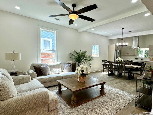 living room featuring beam ceiling, ceiling fan with notable chandelier, and light hardwood / wood-style floors