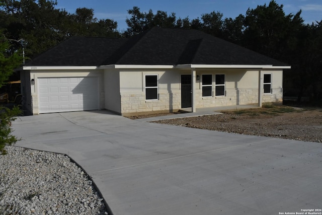 single story home featuring an attached garage, driveway, stone siding, roof with shingles, and stucco siding