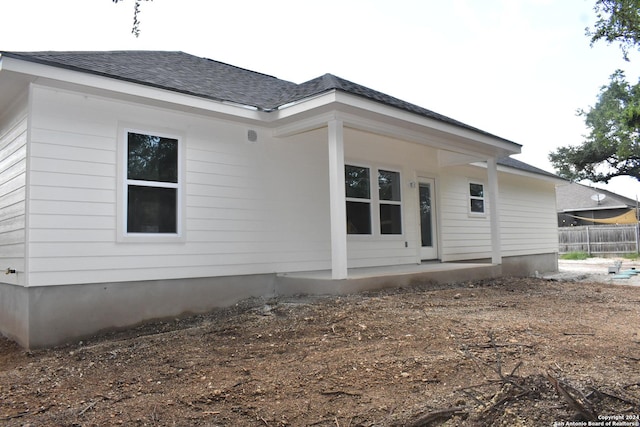 back of property with a shingled roof and fence