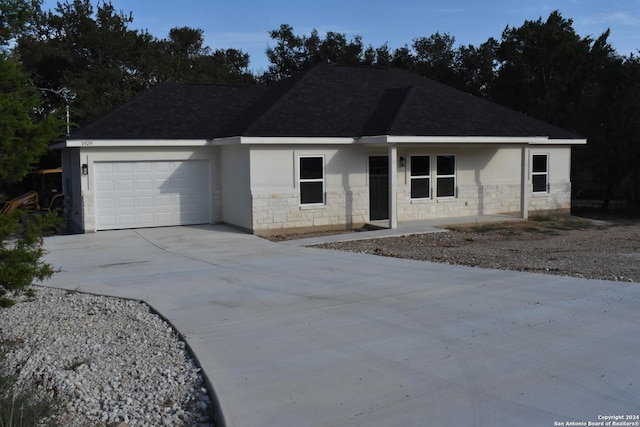 single story home with a garage, driveway, stone siding, roof with shingles, and stucco siding