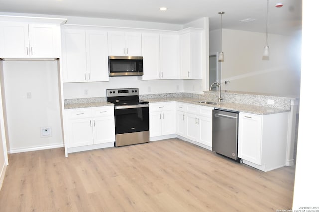 kitchen featuring light wood-style flooring, stainless steel appliances, a sink, white cabinetry, and hanging light fixtures