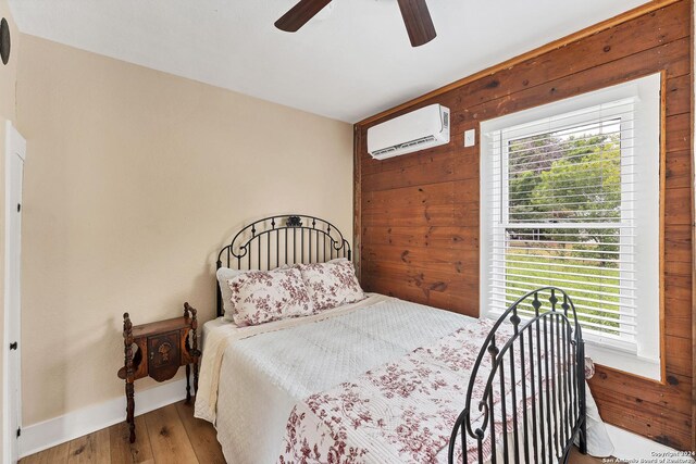 bedroom with wooden walls, a wall mounted AC, hardwood / wood-style floors, and ceiling fan