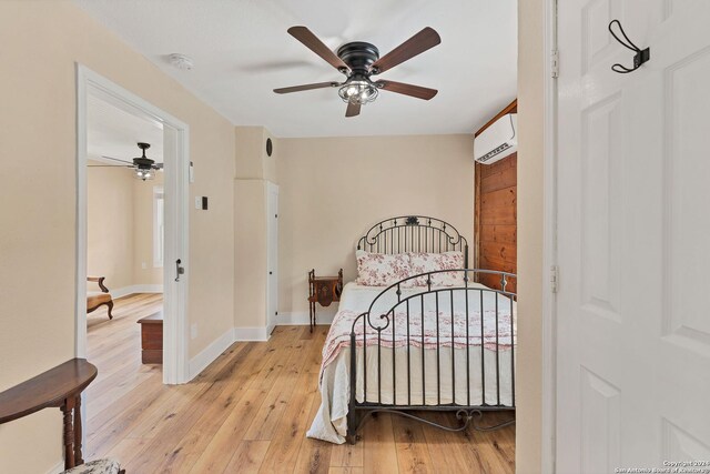 bedroom featuring a wall mounted air conditioner, light wood-type flooring, and ceiling fan