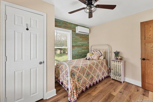 bedroom with light hardwood / wood-style floors, a wall unit AC, and ceiling fan