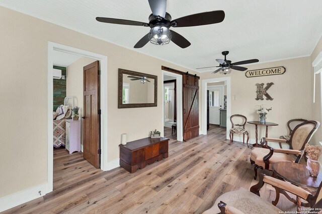 living area featuring light wood-type flooring, ceiling fan, and a barn door