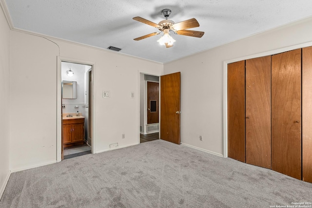 unfurnished bedroom featuring ensuite bathroom, a textured ceiling, carpet flooring, a closet, and ceiling fan