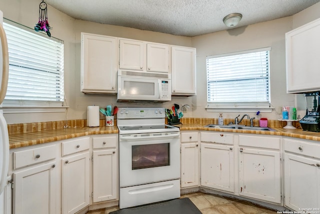 kitchen with sink, white cabinetry, a textured ceiling, white appliances, and a healthy amount of sunlight