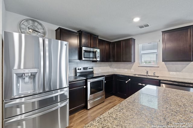 kitchen featuring stainless steel appliances, sink, light stone counters, backsplash, and light wood-type flooring