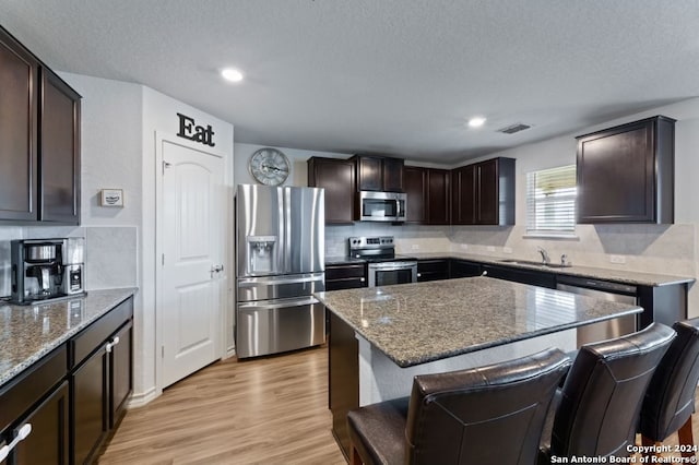 kitchen featuring backsplash, light hardwood / wood-style floors, stone counters, and appliances with stainless steel finishes