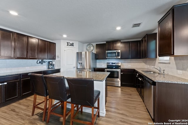 kitchen featuring appliances with stainless steel finishes, sink, light stone counters, light hardwood / wood-style floors, and a kitchen breakfast bar