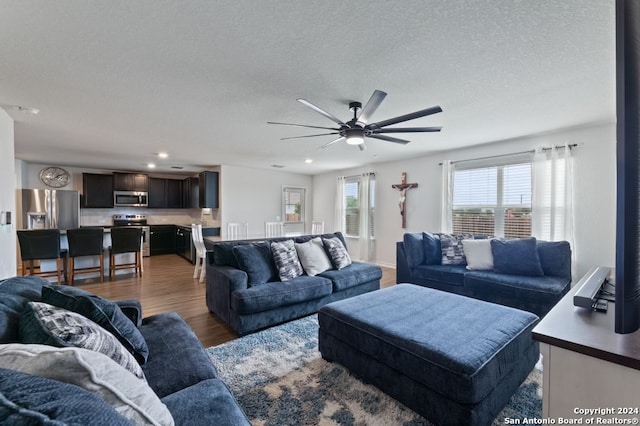 living room with a textured ceiling, ceiling fan, and hardwood / wood-style floors