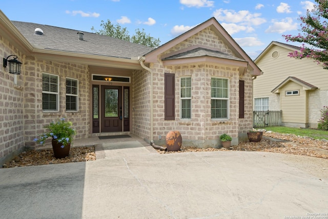 view of exterior entry with stone siding and a shingled roof