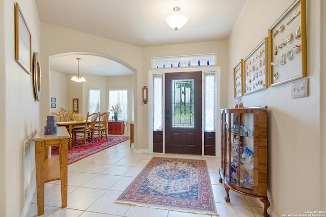 foyer entrance featuring light tile patterned floors, a chandelier, arched walkways, and baseboards