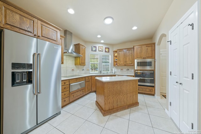 kitchen featuring wall chimney exhaust hood, a center island, stainless steel appliances, light countertops, and a warming drawer