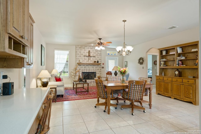 dining room featuring light tile patterned floors, visible vents, arched walkways, a brick fireplace, and ceiling fan with notable chandelier