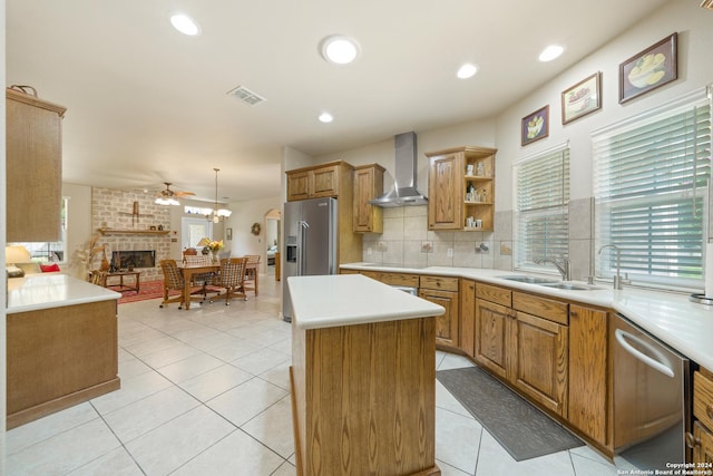 kitchen with stainless steel appliances, light countertops, hanging light fixtures, a kitchen island, and wall chimney range hood