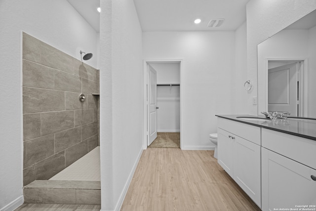 bathroom with a tile shower, vanity, hardwood / wood-style flooring, and toilet