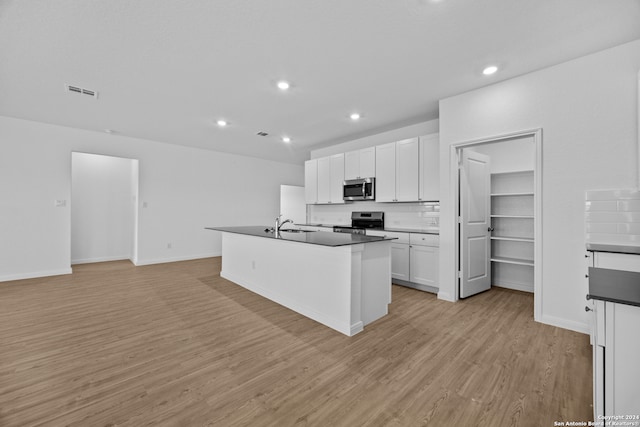 kitchen with appliances with stainless steel finishes, white cabinets, decorative backsplash, light wood-type flooring, and a kitchen island with sink