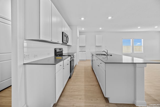 kitchen with stainless steel appliances, white cabinets, sink, light hardwood / wood-style floors, and a kitchen island with sink