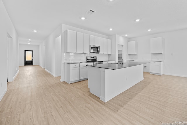 kitchen featuring appliances with stainless steel finishes, white cabinetry, light wood-type flooring, and a kitchen island with sink