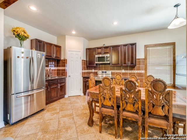 kitchen featuring stainless steel appliances, sink, hanging light fixtures, backsplash, and light tile patterned flooring