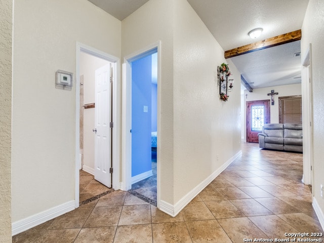 corridor featuring beam ceiling and light tile patterned floors