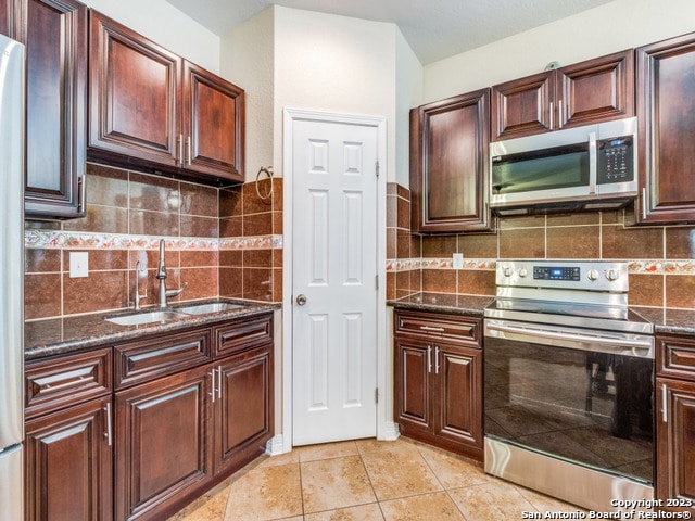 kitchen featuring light tile patterned floors, dark stone counters, backsplash, stainless steel appliances, and sink