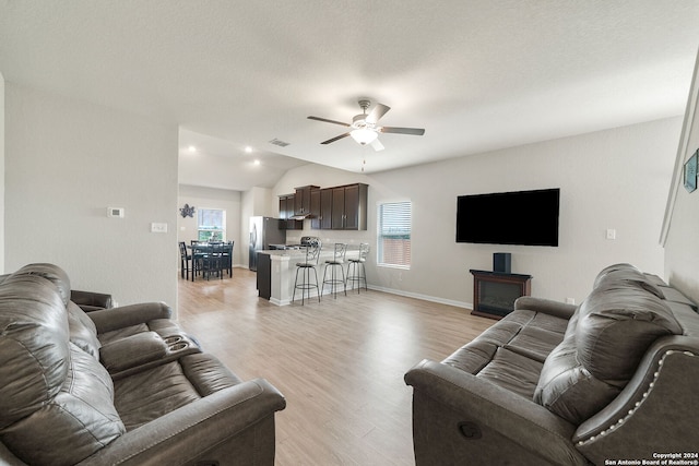 living room featuring vaulted ceiling, a textured ceiling, ceiling fan, and light hardwood / wood-style floors