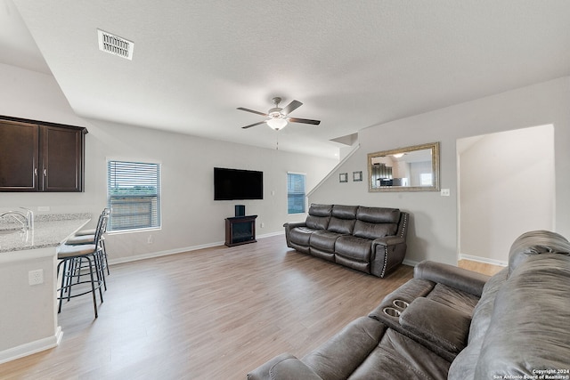 living room featuring ceiling fan, sink, a textured ceiling, and light wood-type flooring