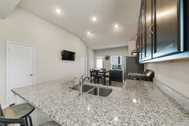 kitchen with lofted ceiling, sink, range, light stone counters, and a kitchen bar