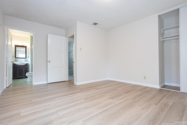 unfurnished bedroom featuring a closet, ensuite bathroom, a textured ceiling, and light wood-type flooring