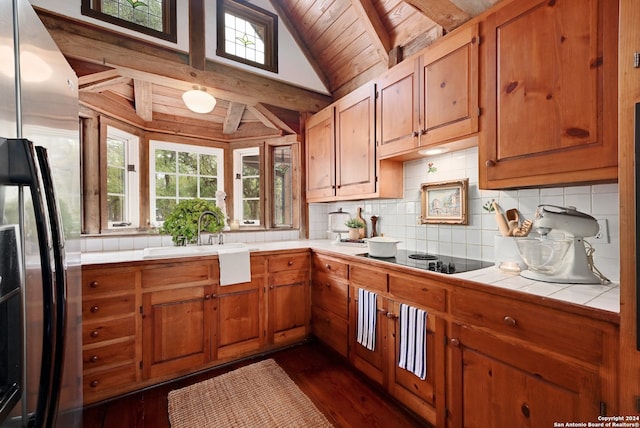 kitchen with dark wood-type flooring, wooden ceiling, tile counters, stainless steel fridge, and black electric stovetop