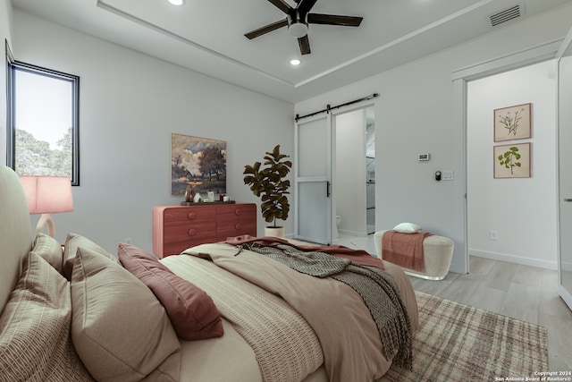 bedroom with light wood-type flooring, ceiling fan, and a barn door