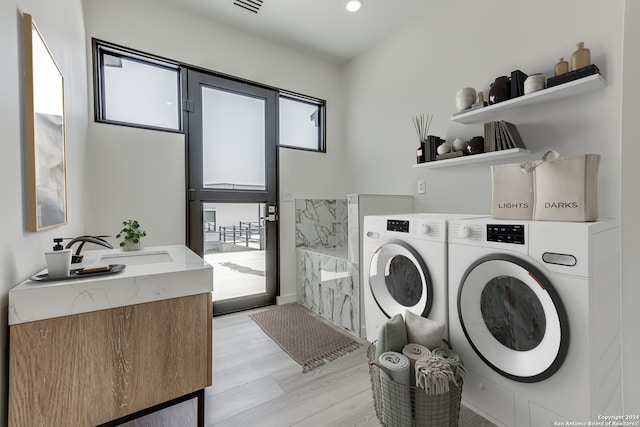 laundry room with washing machine and clothes dryer, sink, and light hardwood / wood-style flooring