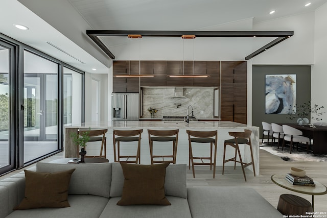 kitchen with stainless steel refrigerator with ice dispenser, sink, light hardwood / wood-style floors, an island with sink, and wall chimney exhaust hood