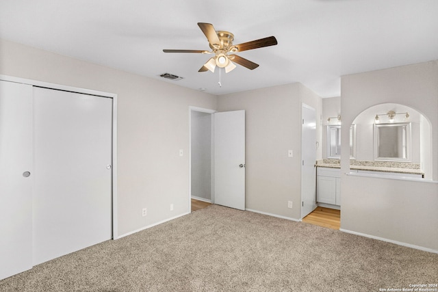 unfurnished bedroom with ceiling fan, light colored carpet, ensuite bathroom, and a closet