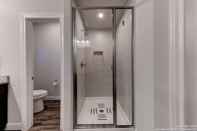 bathroom with wood-type flooring, a shower with shower door, toilet, and vanity