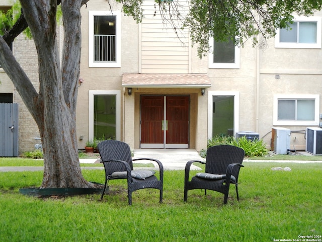 view of exterior entry with a lawn and cooling unit