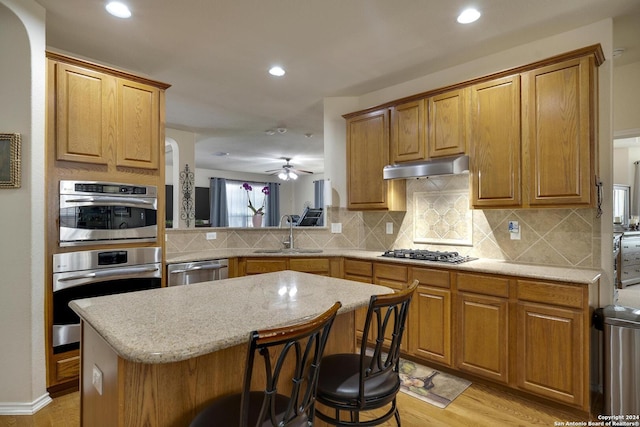 kitchen with appliances with stainless steel finishes, sink, a kitchen breakfast bar, decorative backsplash, and a center island