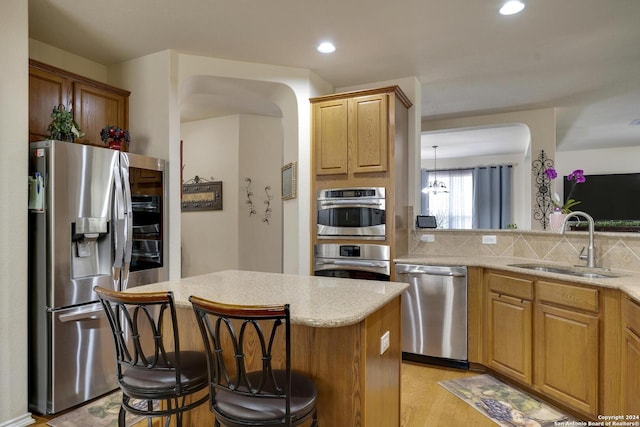 kitchen with a kitchen bar, sink, hanging light fixtures, stainless steel appliances, and backsplash