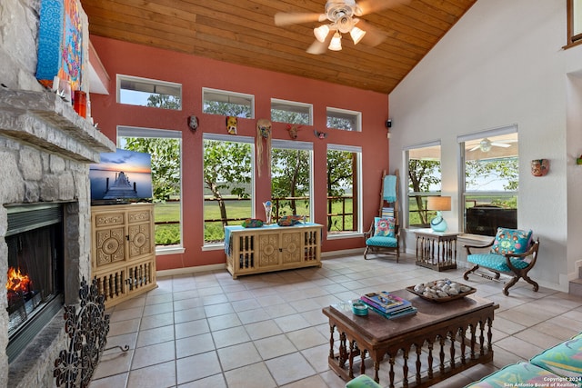 sunroom with ceiling fan, a stone fireplace, vaulted ceiling, and wood ceiling