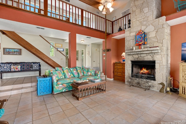 tiled living room featuring ceiling fan, a stone fireplace, and a high ceiling