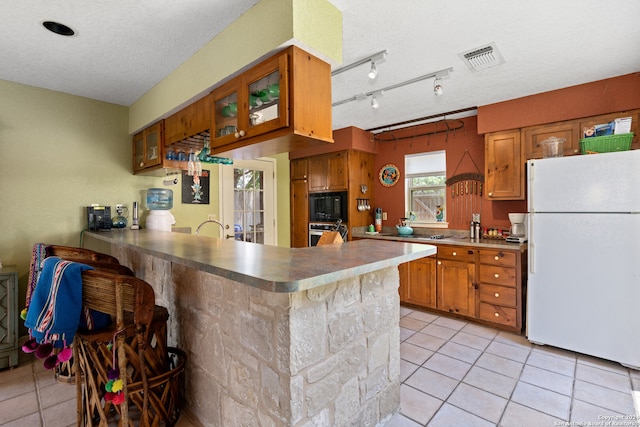 kitchen with stainless steel oven, a textured ceiling, kitchen peninsula, track lighting, and white refrigerator