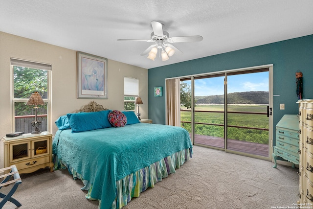 carpeted bedroom featuring access to outside, multiple windows, a textured ceiling, and ceiling fan