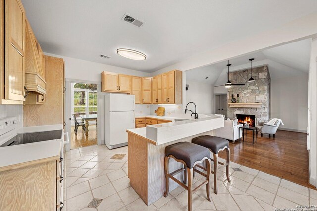 kitchen with light wood-type flooring, vaulted ceiling, kitchen peninsula, a fireplace, and white refrigerator