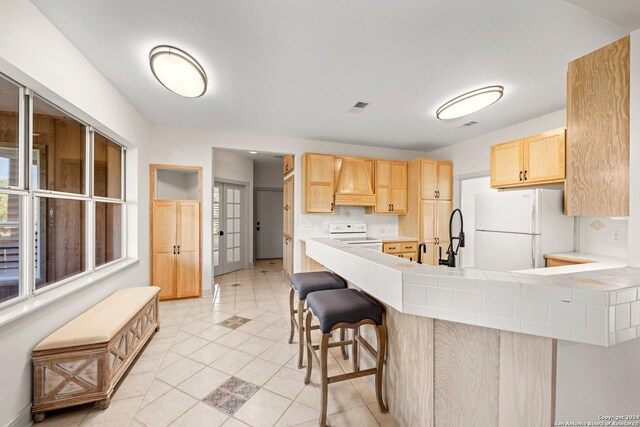 kitchen featuring light brown cabinetry, a kitchen breakfast bar, custom exhaust hood, kitchen peninsula, and white appliances