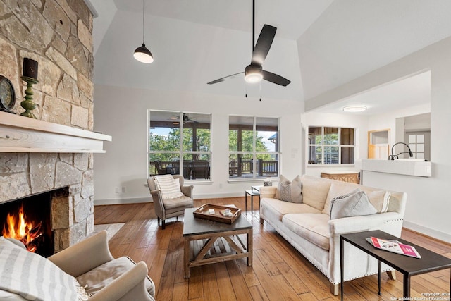 living room featuring a stone fireplace, light wood-type flooring, ceiling fan, and high vaulted ceiling