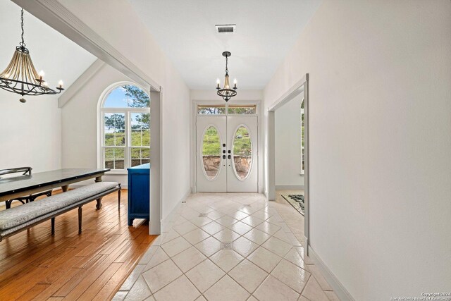 foyer entrance with a notable chandelier, lofted ceiling, french doors, and light wood-type flooring