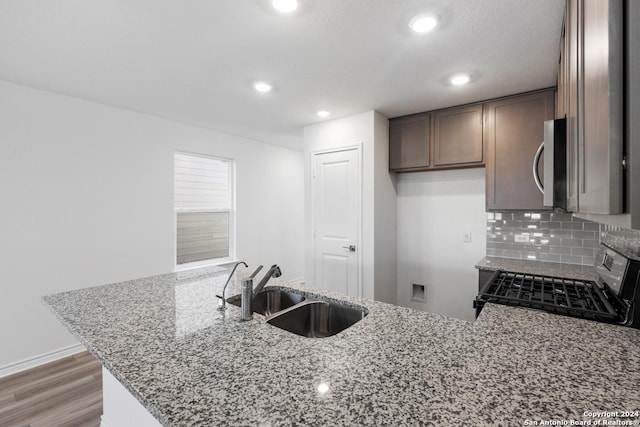 kitchen featuring sink, backsplash, light stone counters, kitchen peninsula, and stainless steel appliances